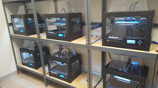 Несколько 3D-принтеров в закрытых корпусах на стеллаже
